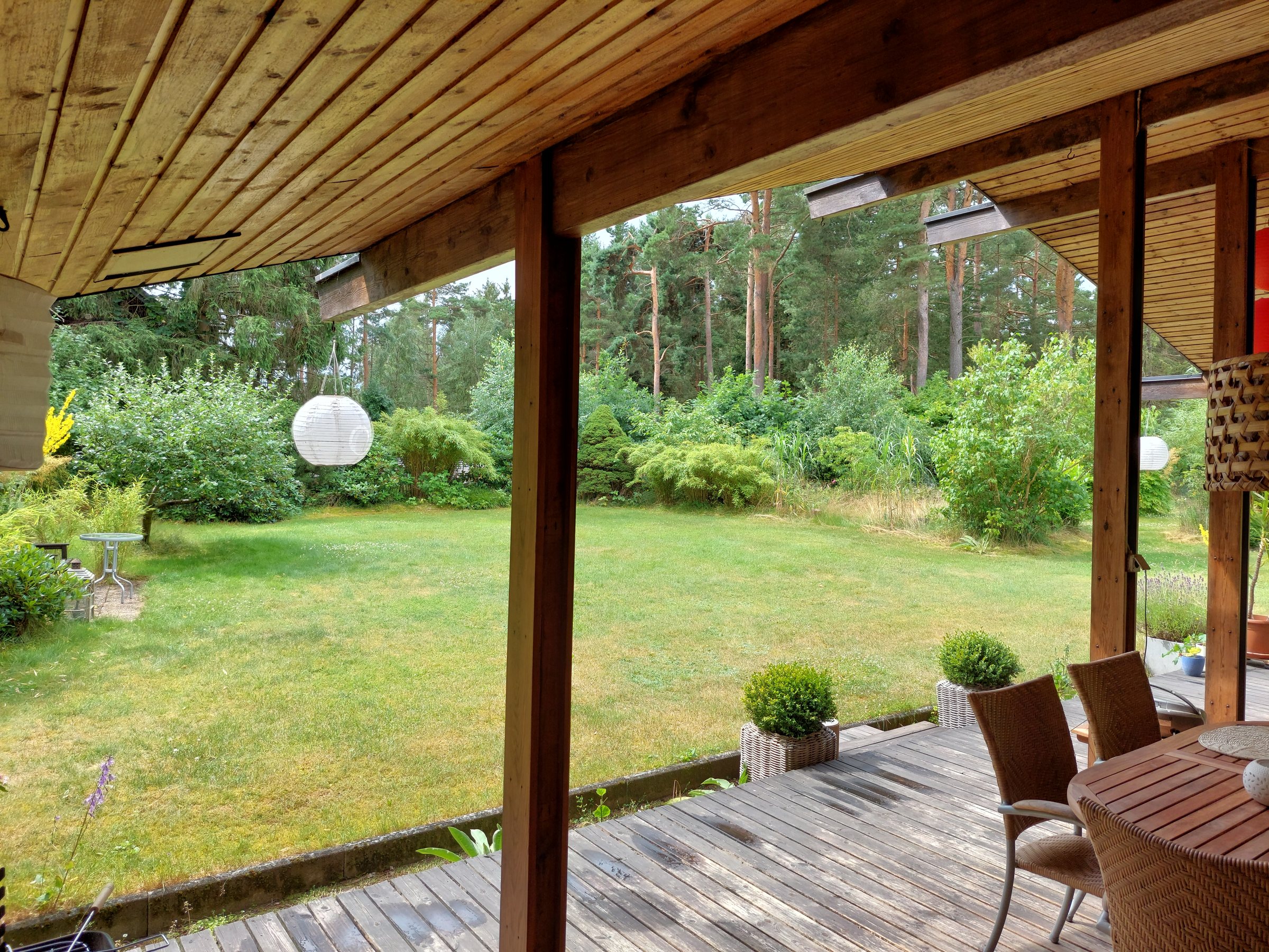Covered deck with lounge seating overlooking the lawn and forest treeline